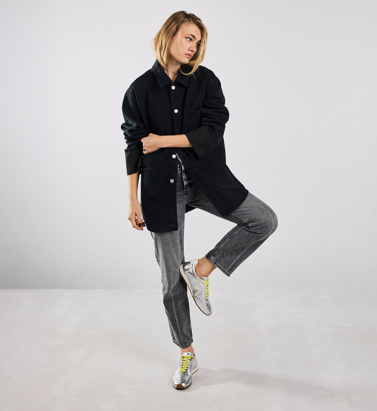 Person wearing a black coat and gray pants on a white background with silver sneakers