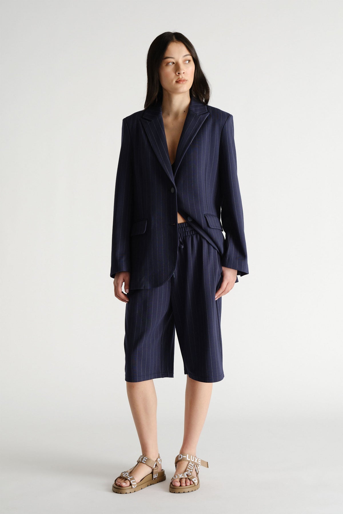 Model wearing a navy pinstripe blazer with tailored shorts and sandals