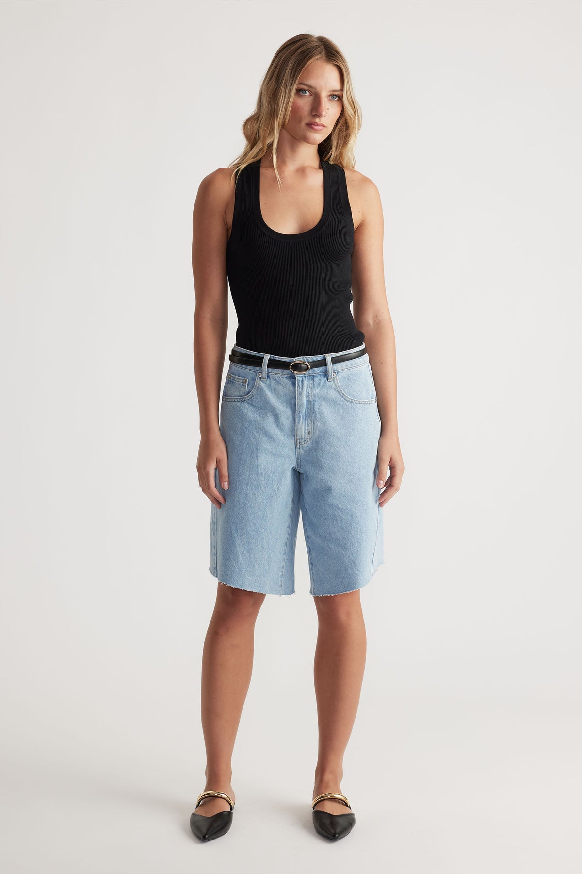 Woman wearing light wash denim shorts paired with a black tank top and pointed black flats for a casual look