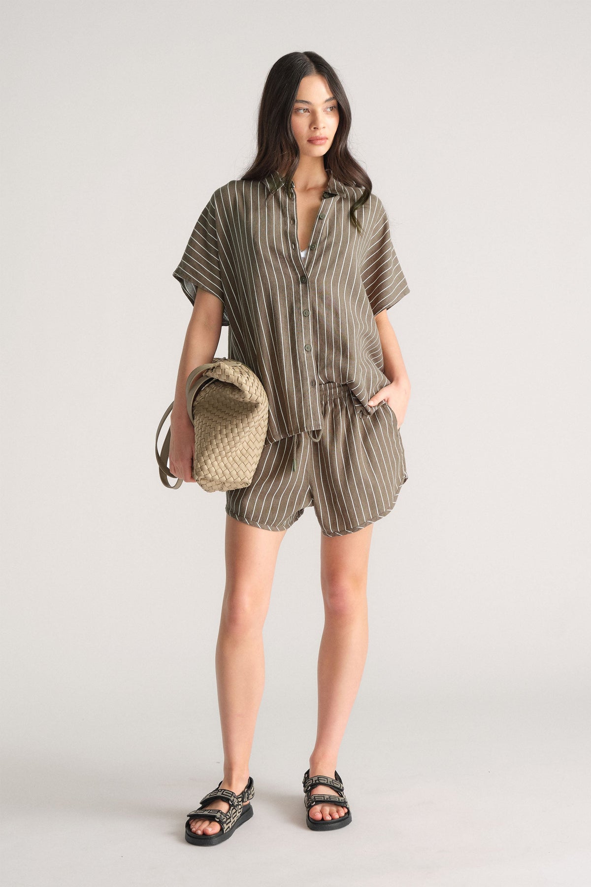 Model wearing D-Luxe Linen Blend Curve Short with striped top and woven bag, first gallery image, portrait orientation.