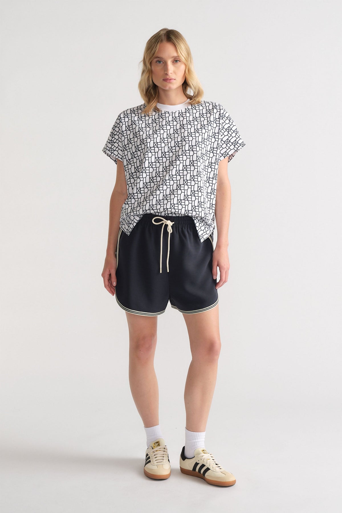 Woman wearing a relaxed black and white monogram tee paired with black drawstring shorts and retro sneakers for casual style.