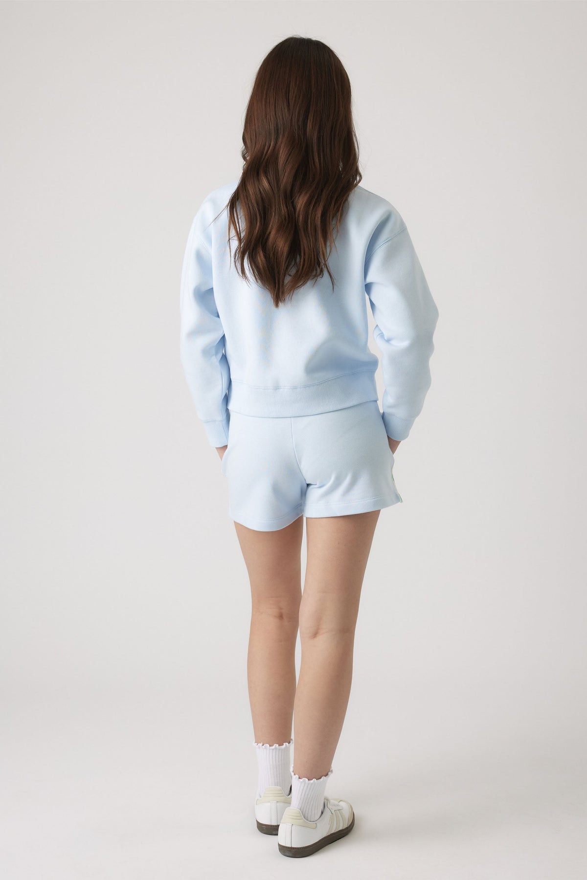 Girl wearing a light blue sweatshirt and matching sweat shorts with sneakers viewed from behind
