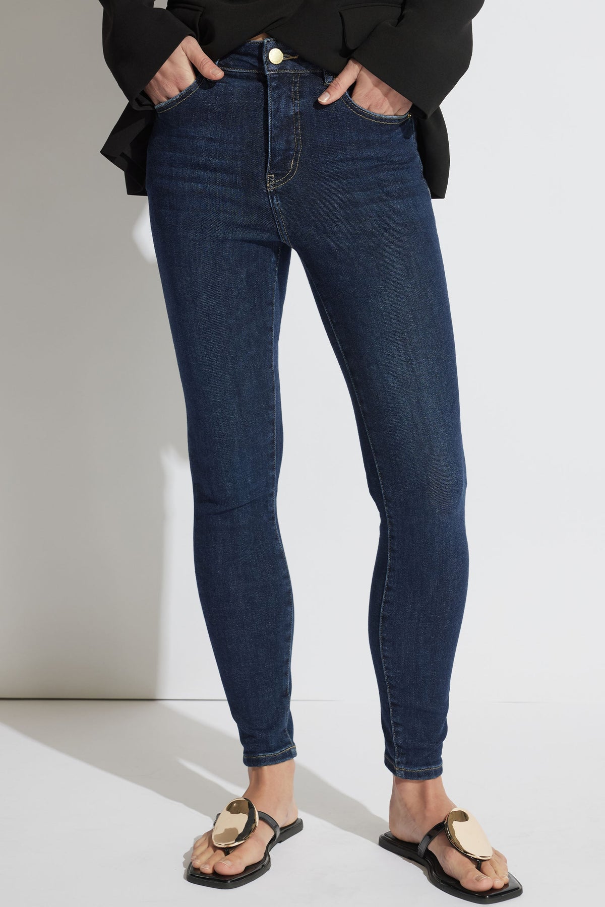 Woman wearing fitted dark blue high-rise skinny jeans styled with a black top and flat sandals for a casual look