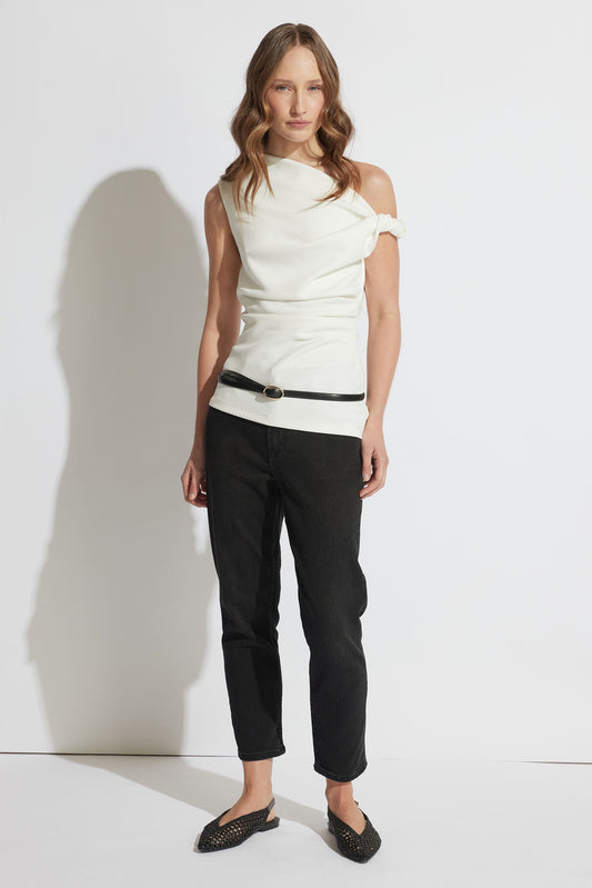 Woman wearing a white sleeveless top and black slim leg cropped jeans against a white background