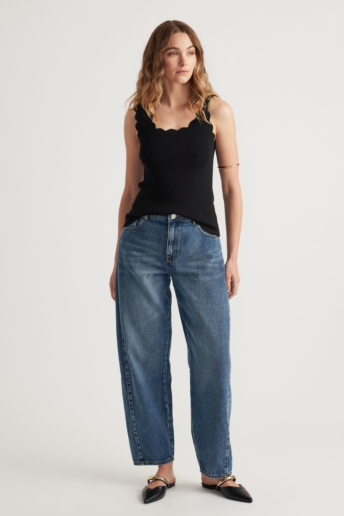 Woman wearing a black scallop edge tank top paired with relaxed fit blue denim jeans and black pointed flats.