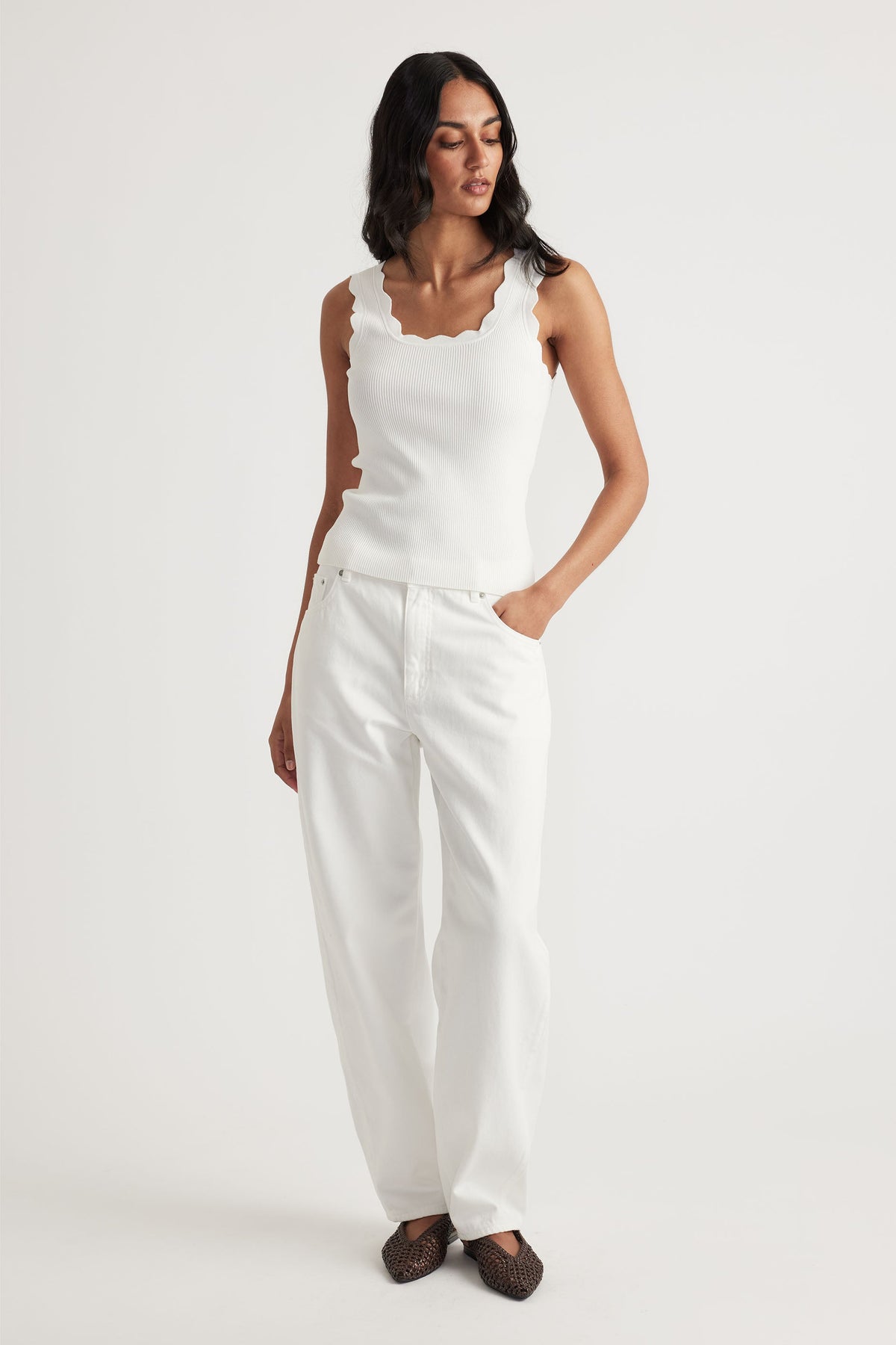 Woman wearing a white scalloped edge ribbed tank top paired with relaxed fit white pants and brown woven shoes