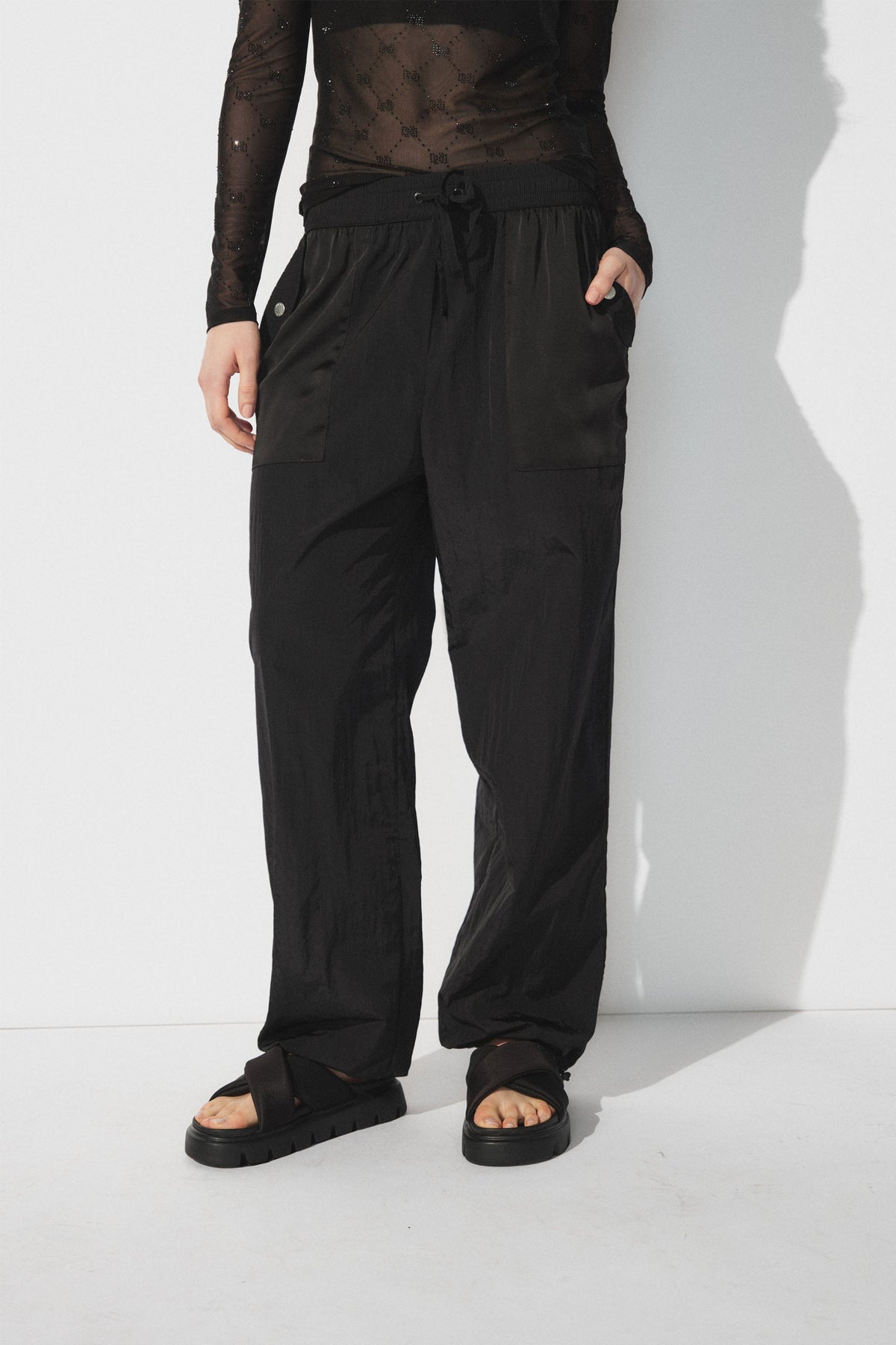 Woman wearing relaxed black parachute joggers with patch pockets and black platform sandals against a white backdrop
