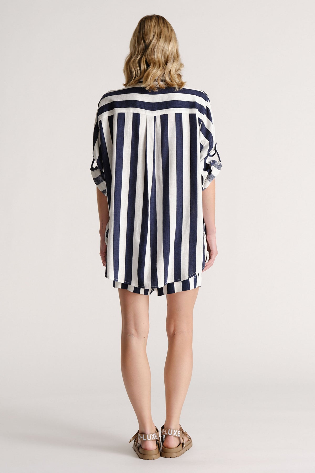 Woman wearing a navy and white vertical striped linen blend shirt with matching shorts and branded tan sandals from behind