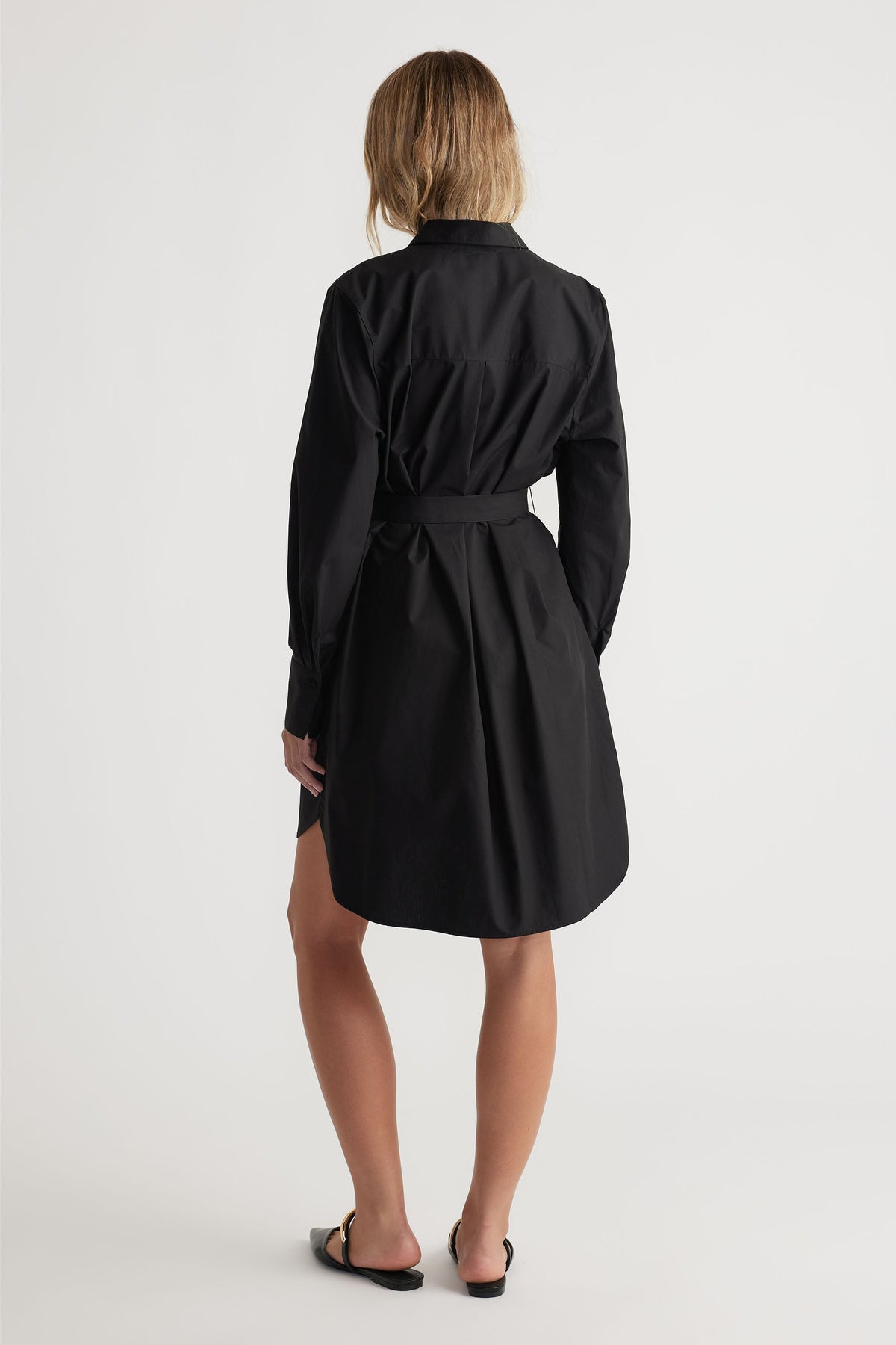Back view of woman wearing a black belted mini shirt dress with long sleeves and a relaxed fit hemline