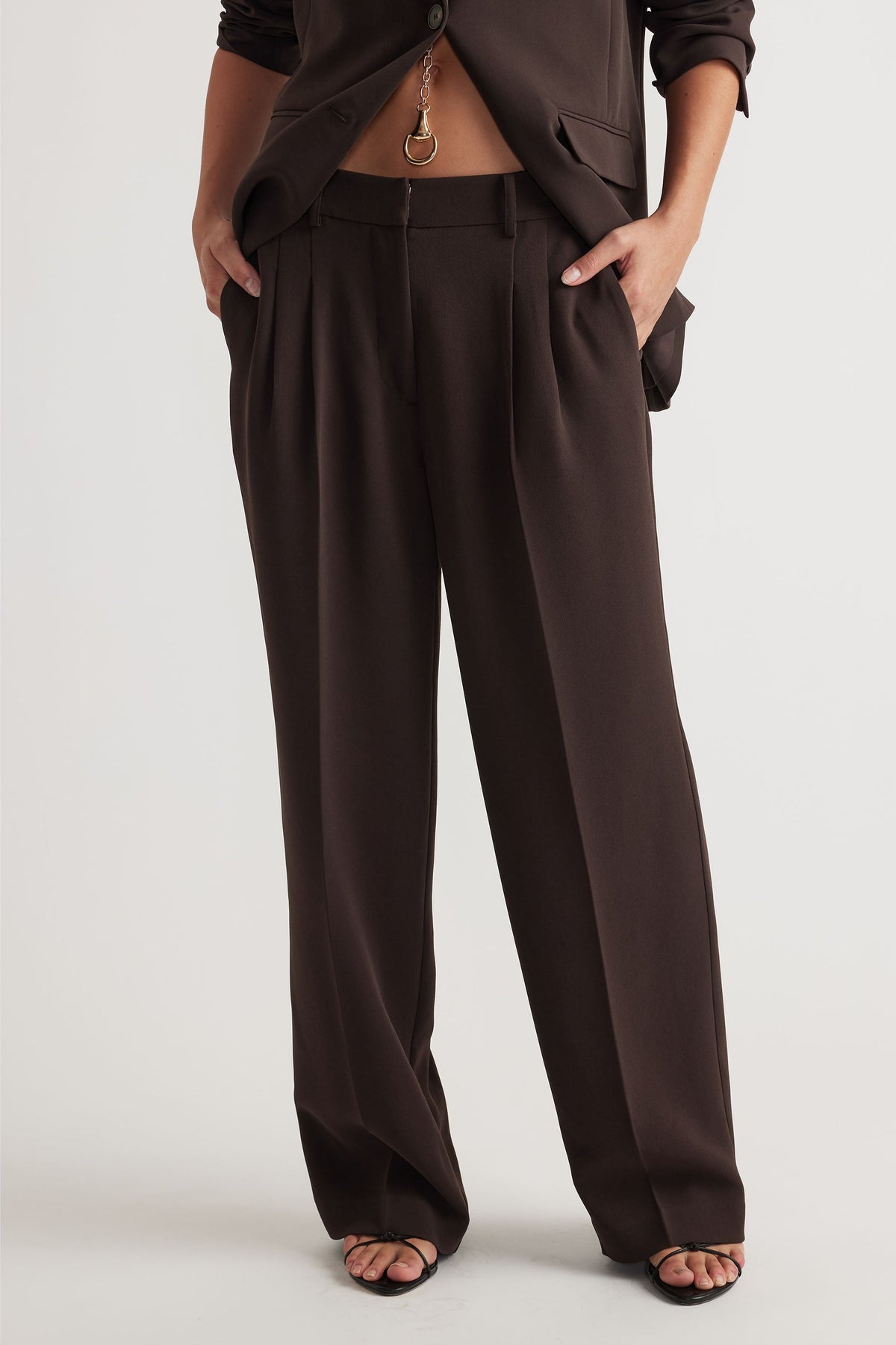 Woman wearing tailored dark brown wide-leg pants with front pleats paired with black strappy sandals and a matching jacket