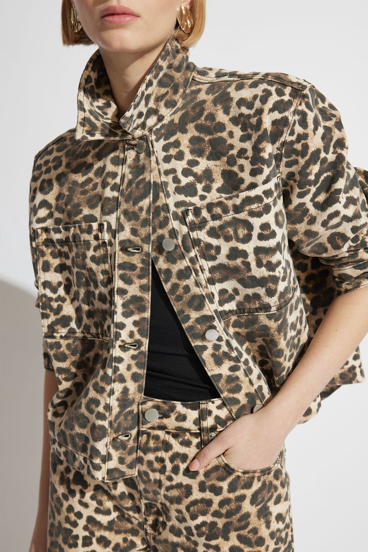 Close-up of a woman wearing a leopard print denim shacket and matching jeans with rolled sleeves and gold hoop earrings