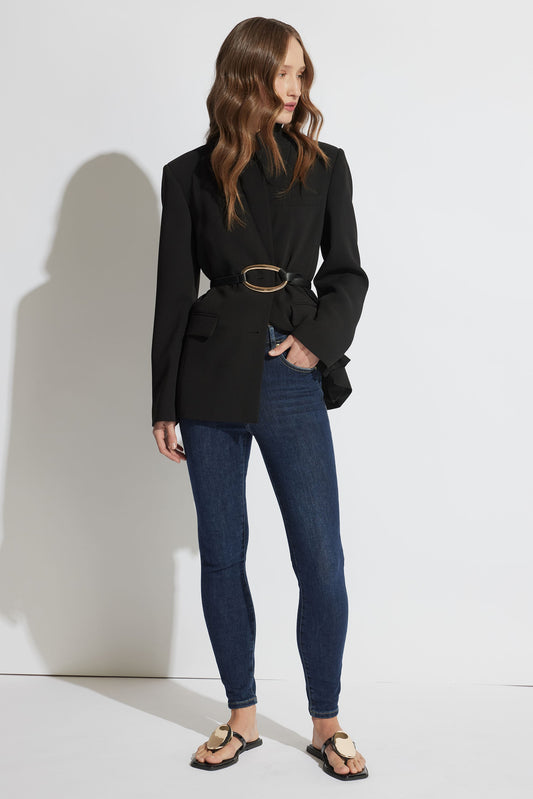 Woman modeling dark blue high-rise skinny jeans styled with a tailored black blazer and minimalist flat sandals