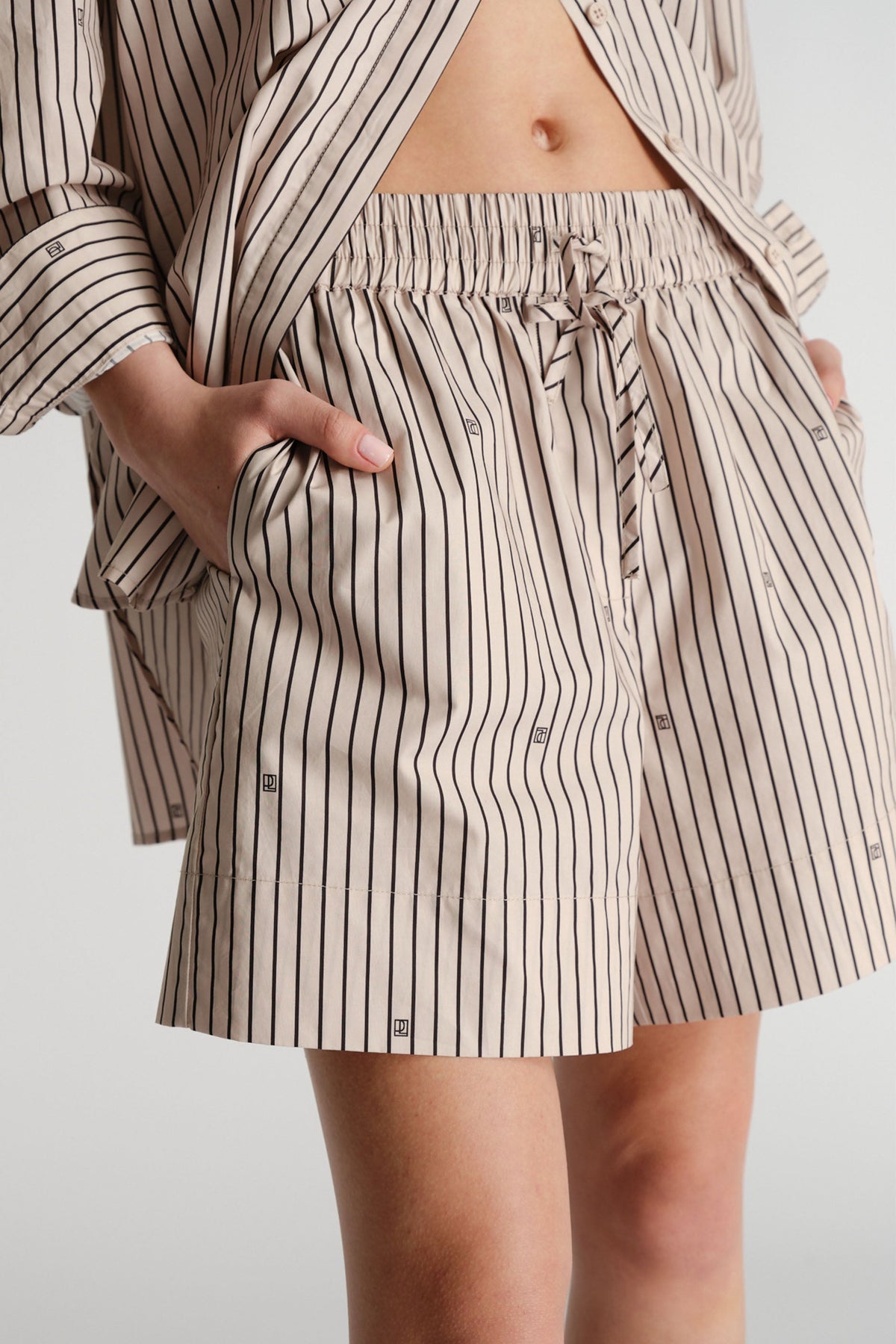 Close-up of woman wearing beige striped shorts with elastic waist and subtle monogram print, paired with matching shirt.
