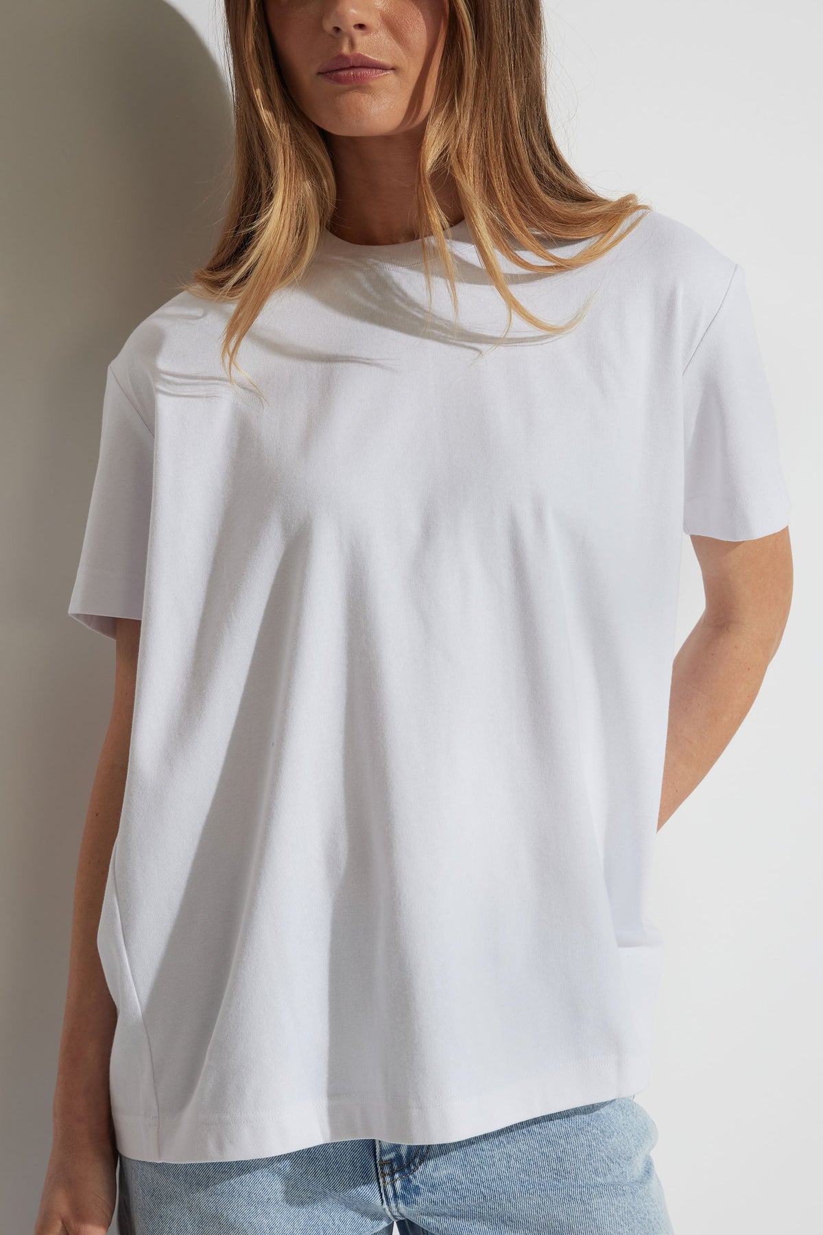 Woman wearing a relaxed white tee with metal detail and light blue denim jeans, styled for effortless everyday wear