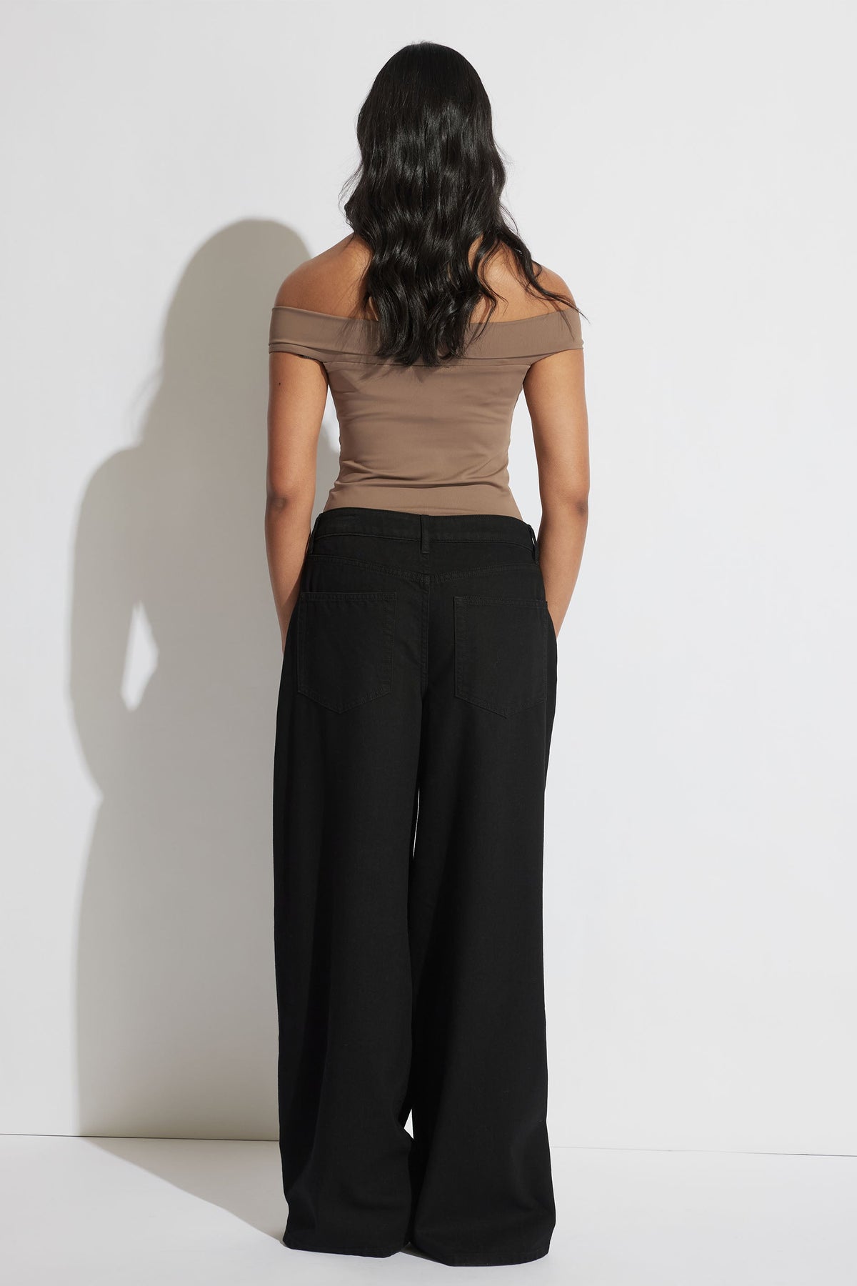 Woman wearing a cappuccino off-shoulder twist top paired with wide-leg black pants, standing against a plain backdrop