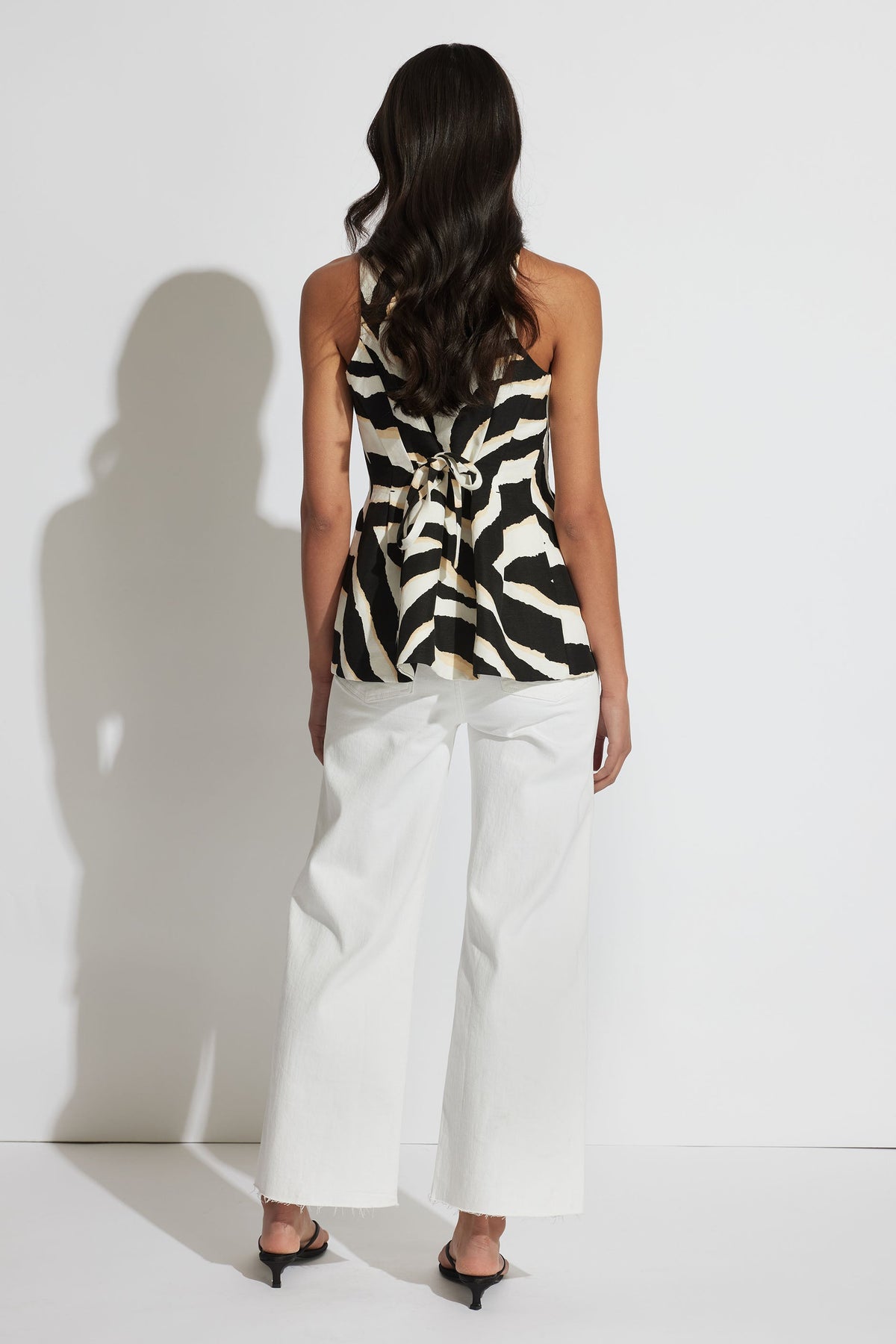Back view of model wearing Veronica Vest Top with adjustable belt and flared waist in black and white print