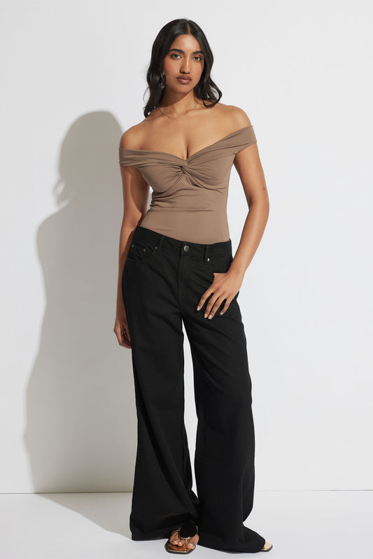 Woman wearing a taupe off-shoulder twist top paired with wide-leg black pants and sandals for a sleek look
