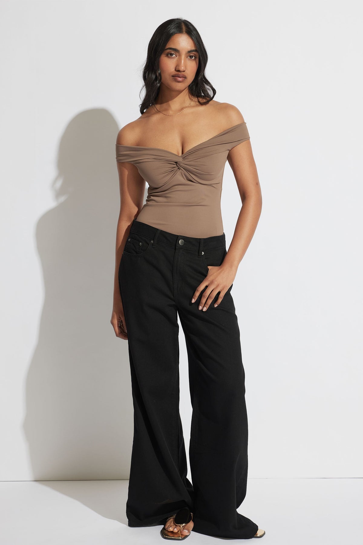 Woman wearing a taupe off-shoulder twist top paired with wide-leg black pants and sandals for a sleek look