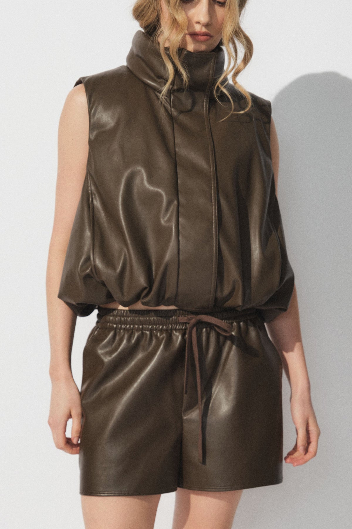 Woman wearing a sleeveless faux leather padded vest with matching brown faux leather shorts in a relaxed fit