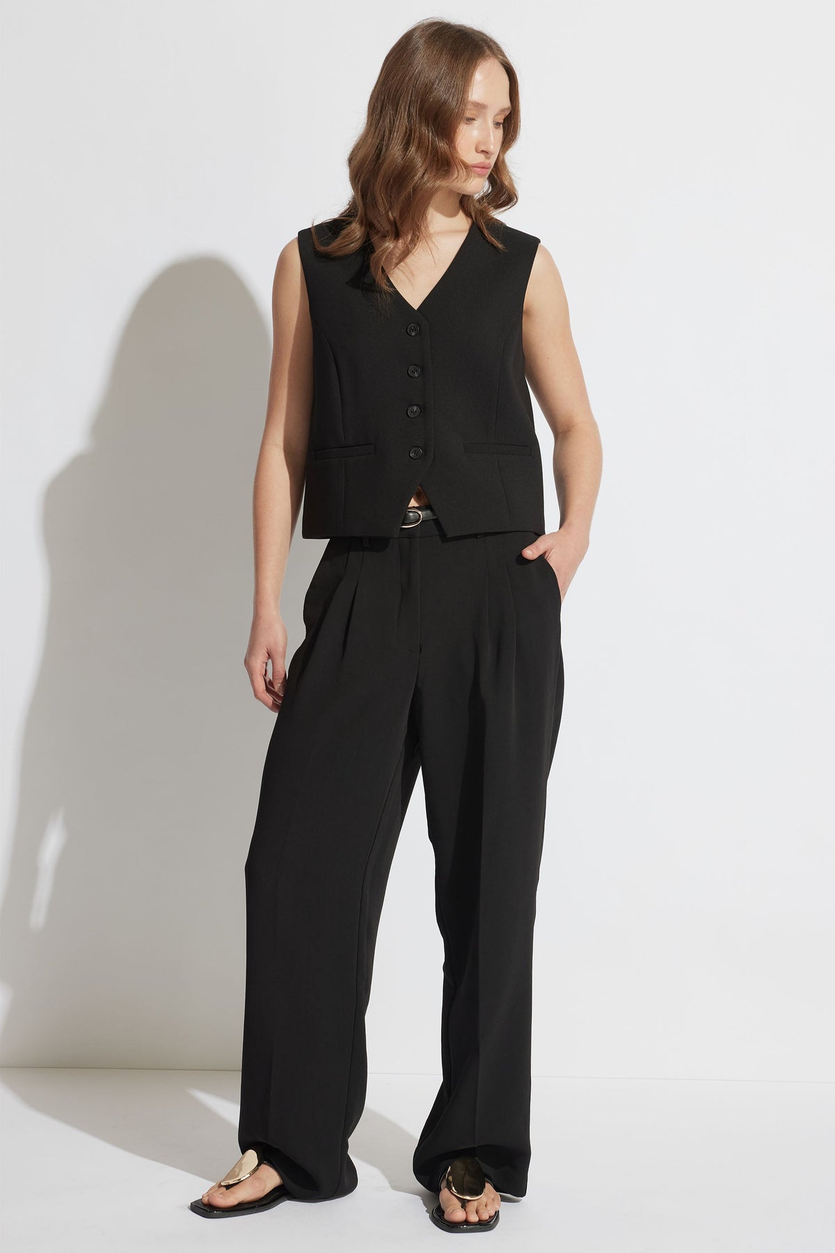 Woman wearing a black tailored vest with a V-neck and button front paired with wide-leg black trousers and sandals