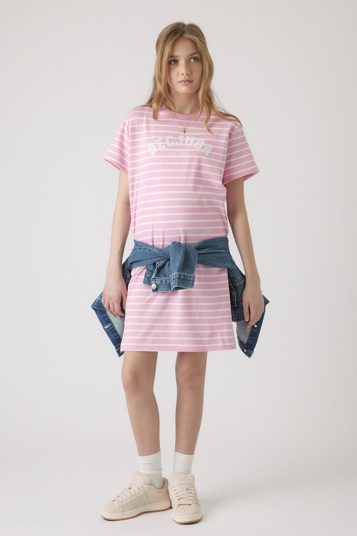 Girl wearing a relaxed pink and white striped rugby tee dress with a tied denim jacket and casual sneakers