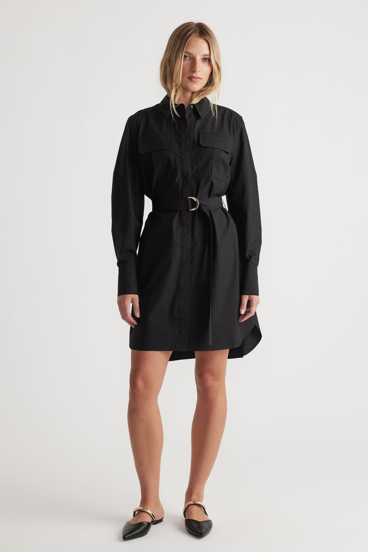 Woman wearing a black belted mini shirt dress with long sleeves and pointed flats for a sleek, modern look