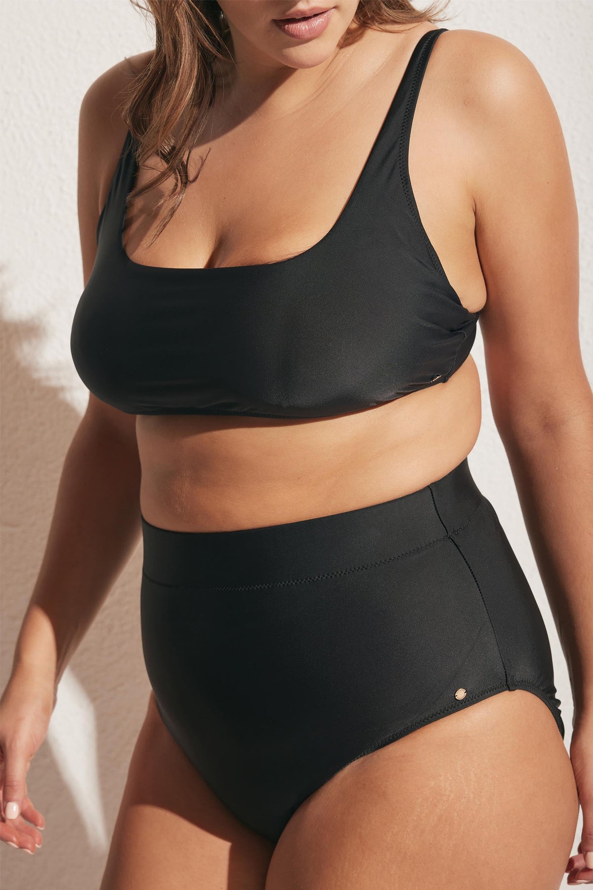 Woman wearing a black matte square neck bikini top with high-waisted matching bottoms in natural sunlight