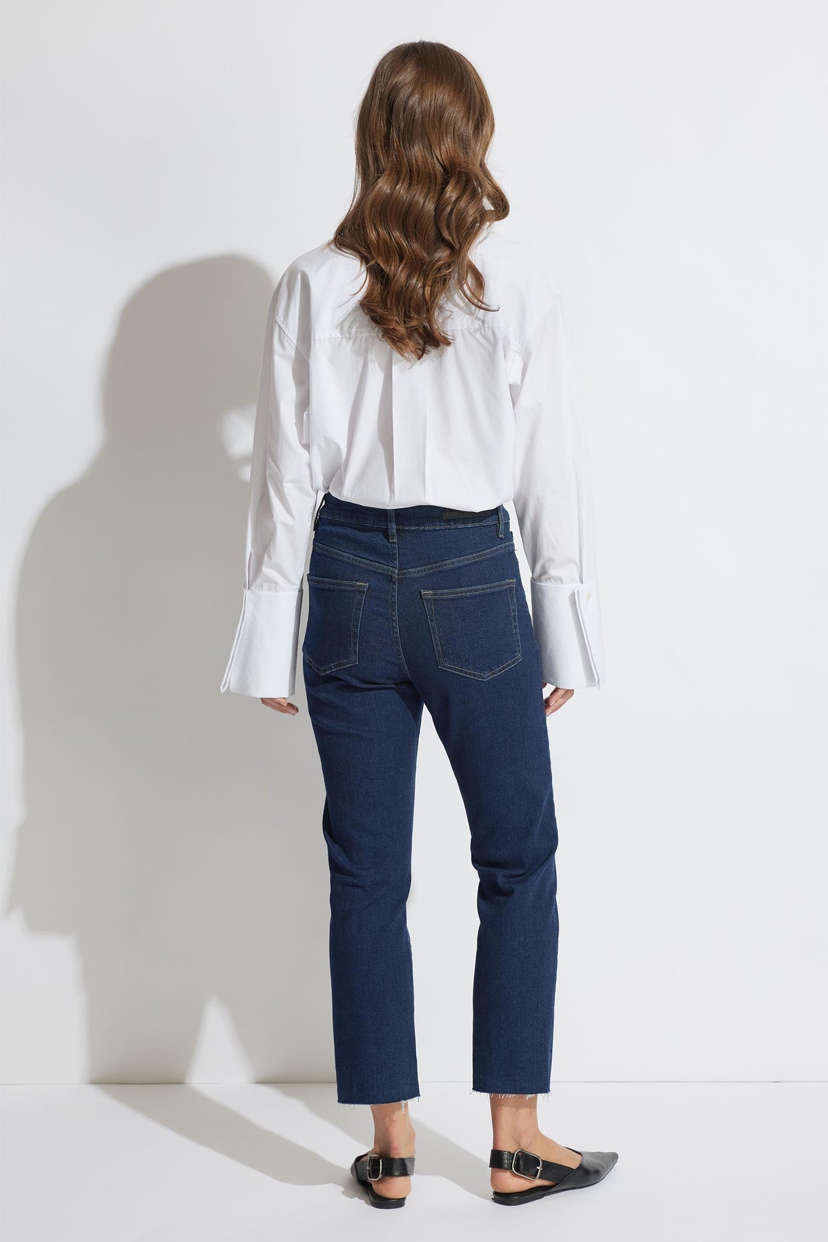 Back view of model wearing Becky Straight Leg Jean in dark denim with raw hem, paired with white shirt, gallery 3 portrait.