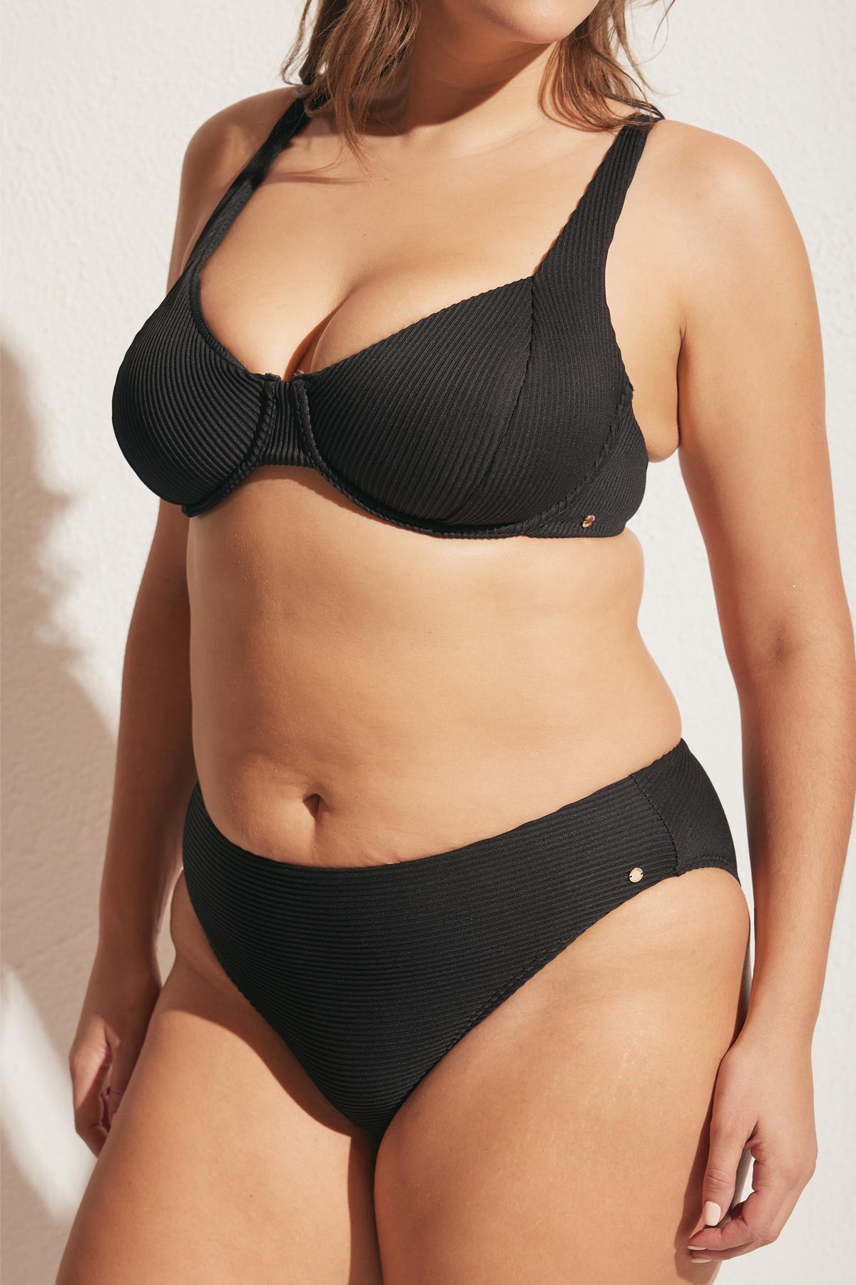 Woman wearing a black ribbed bikini set with supportive underwire top and classic high-rise bottoms in soft natural light