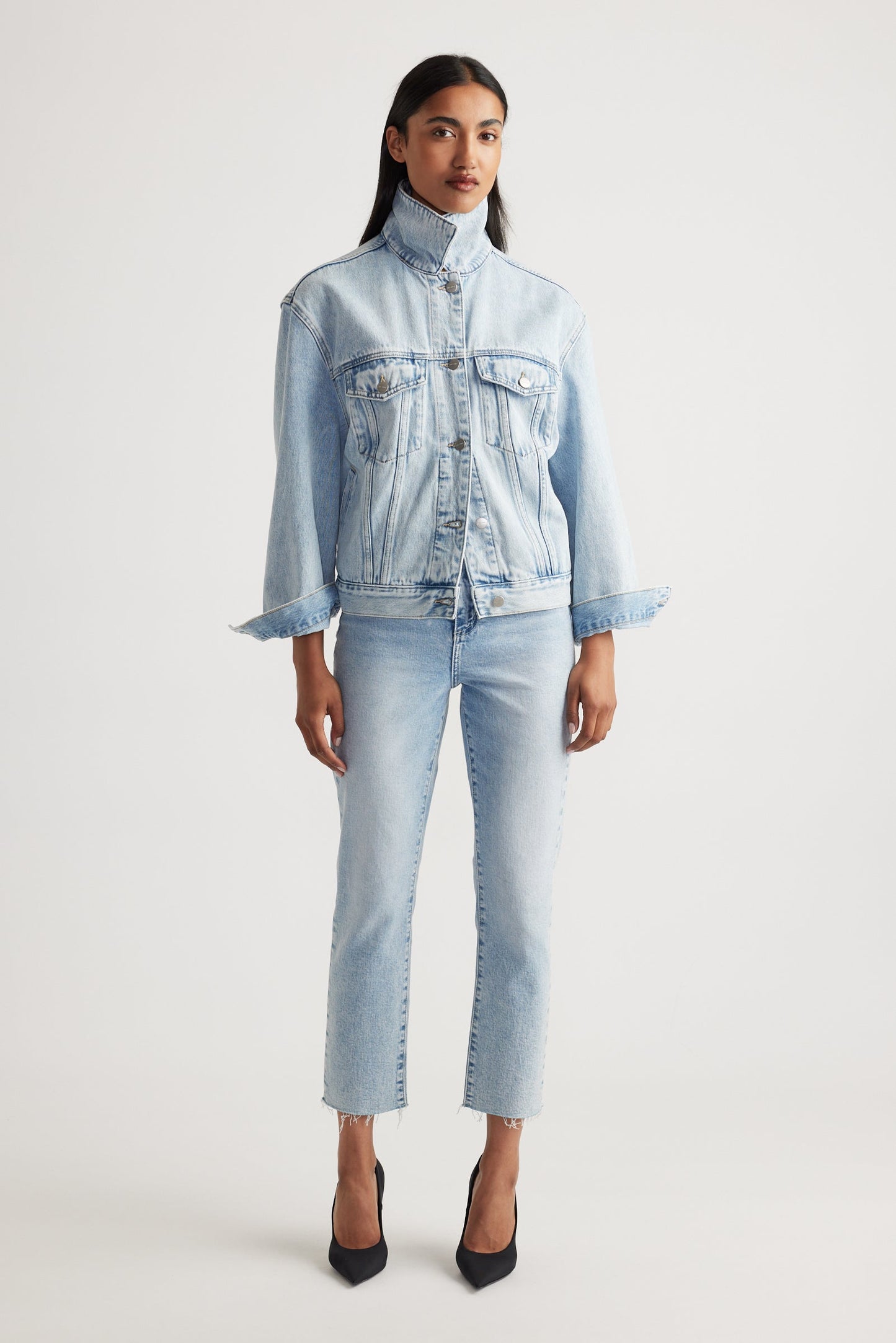 Woman wearing a light blue denim jacket and cropped straight jeans on a white background