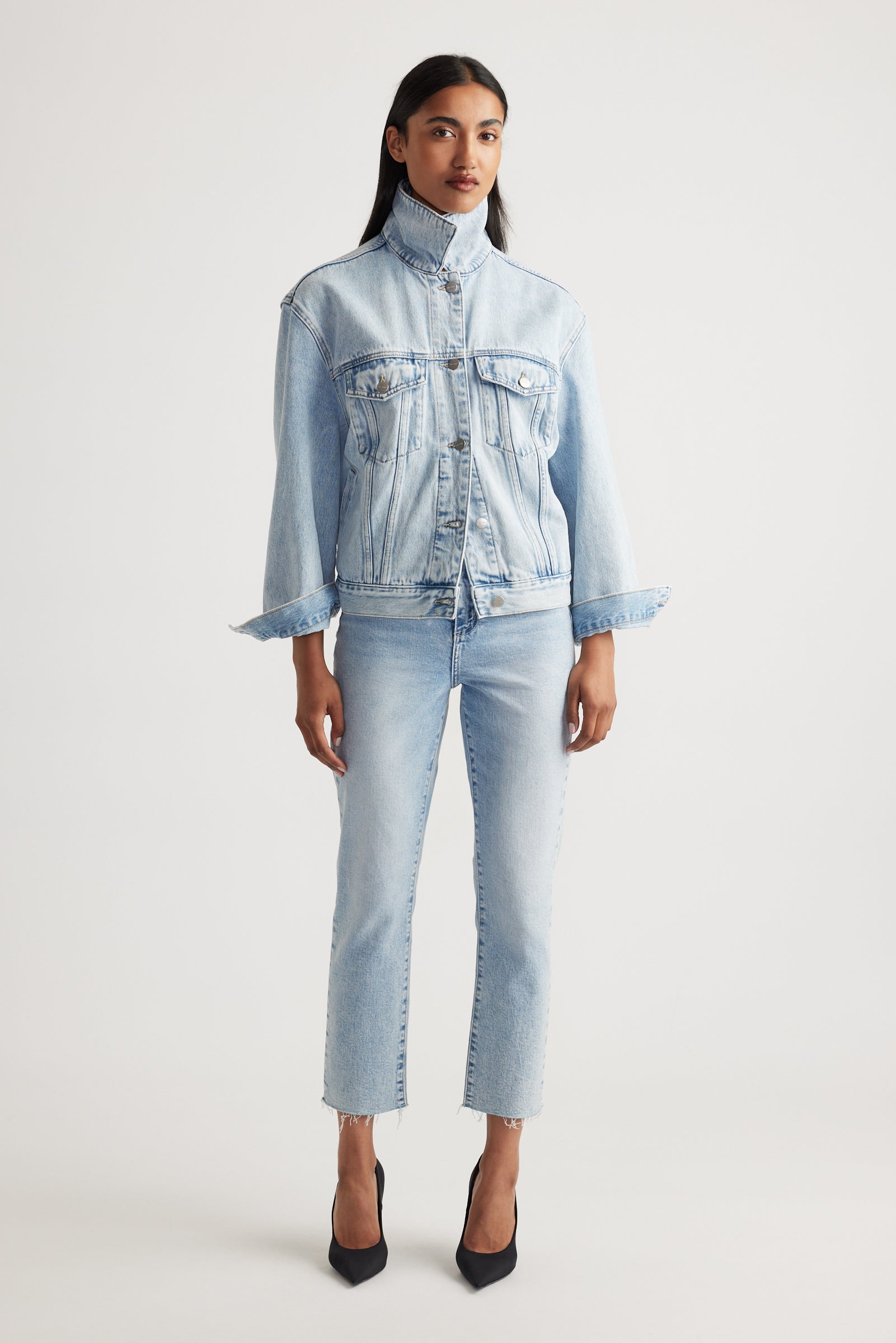 Woman wearing a light blue denim jacket and cropped straight jeans on a white background