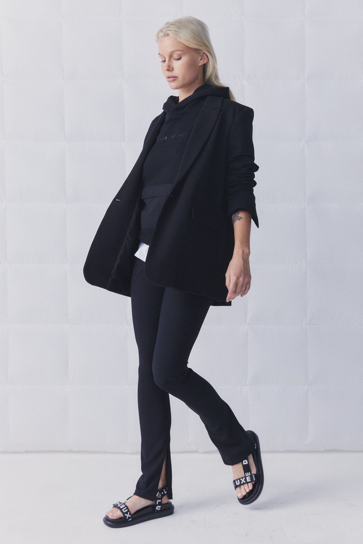 Woman wearing black slim-fit ribbed leggings with side splits paired with a layered black blazer and hoodie ensemble