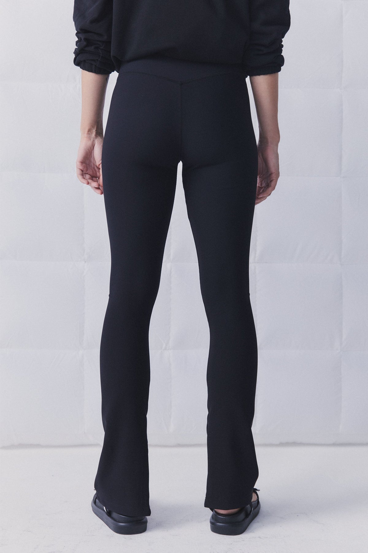 Rear view of black ribbed leggings with a subtle split hem, styled with a relaxed black top and flats