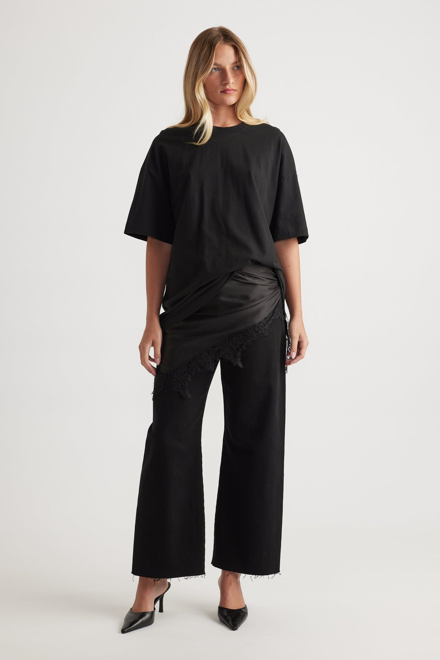 Woman wearing a black oversized tee with black wide-leg high rise cropped jeans on a white background