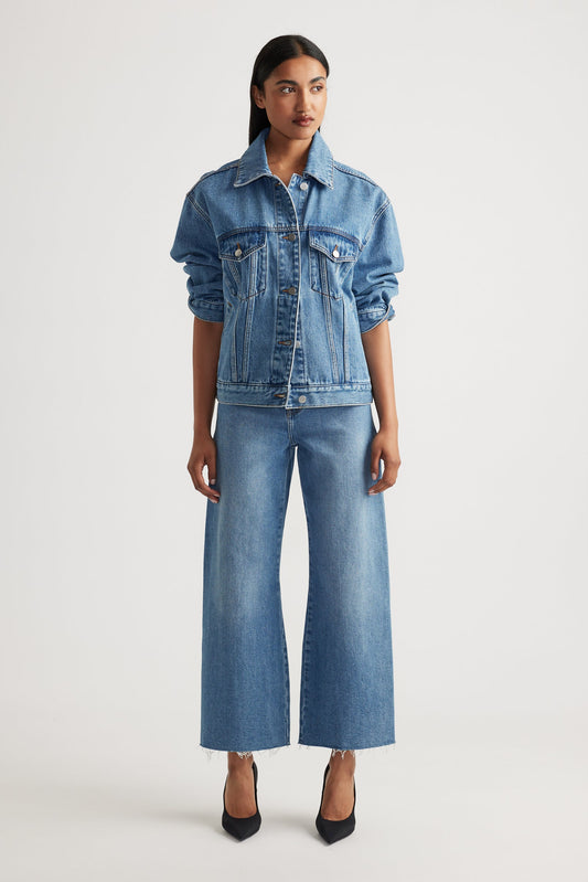 Woman wearing a mid wash blue denim jacket and high rise wide leg cropped jeans on a white background