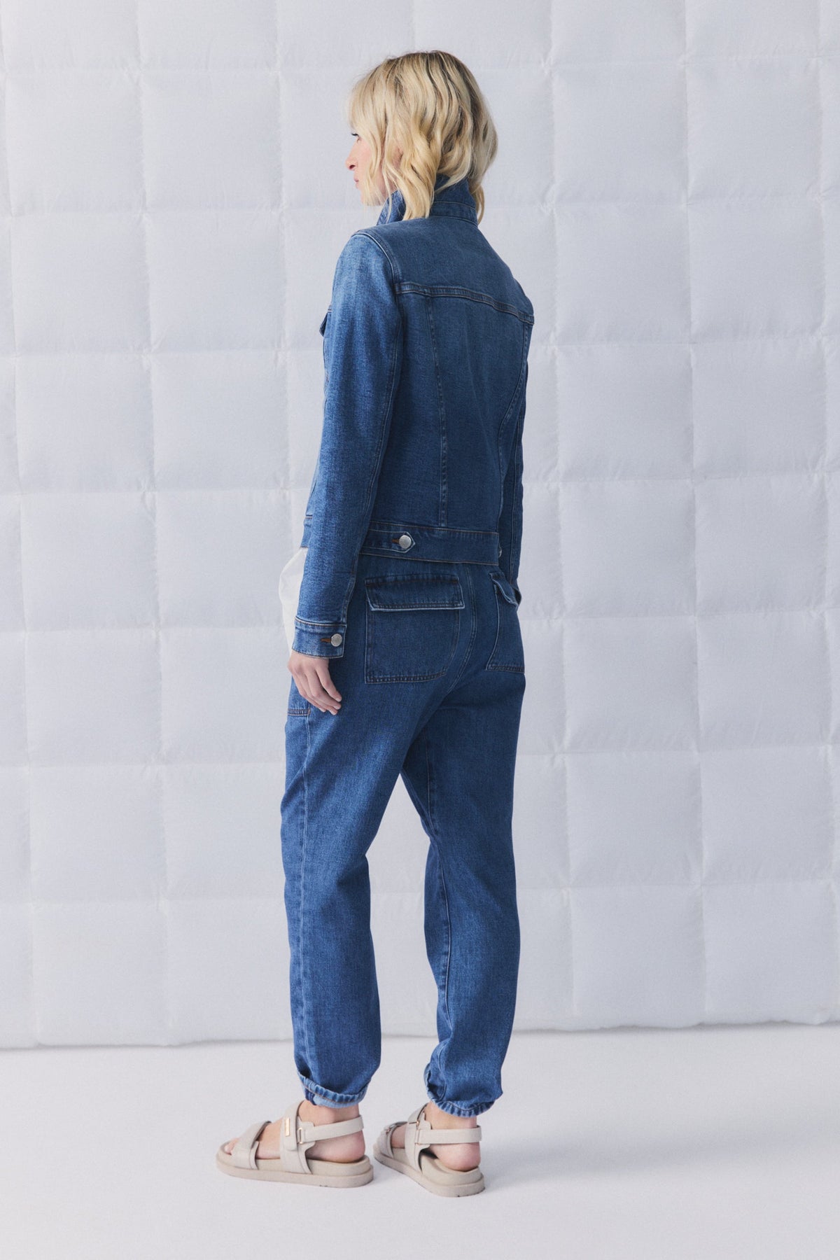 Woman wearing relaxed fit denim joggers and matching denim jacket, styled casually with beige sandals.