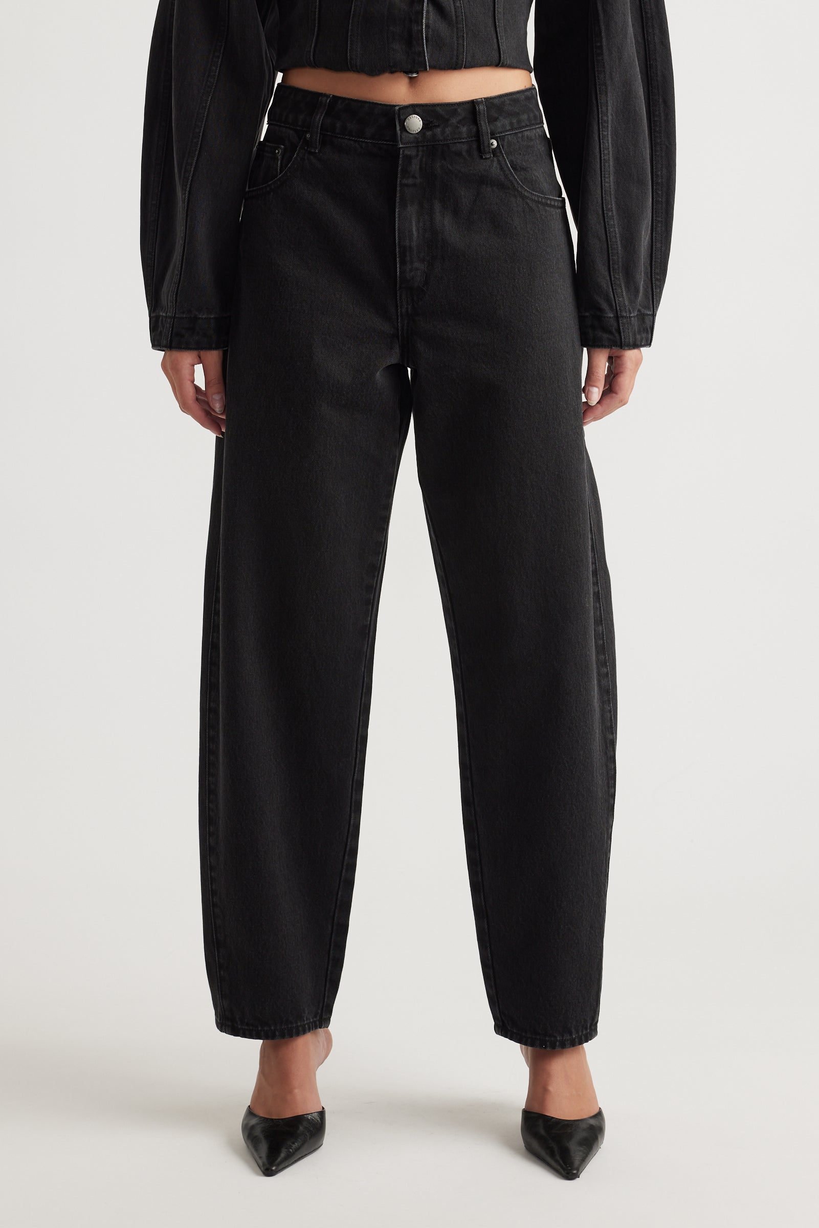 Person wearing black high-waisted barrel jeans and a black jacket on a white background