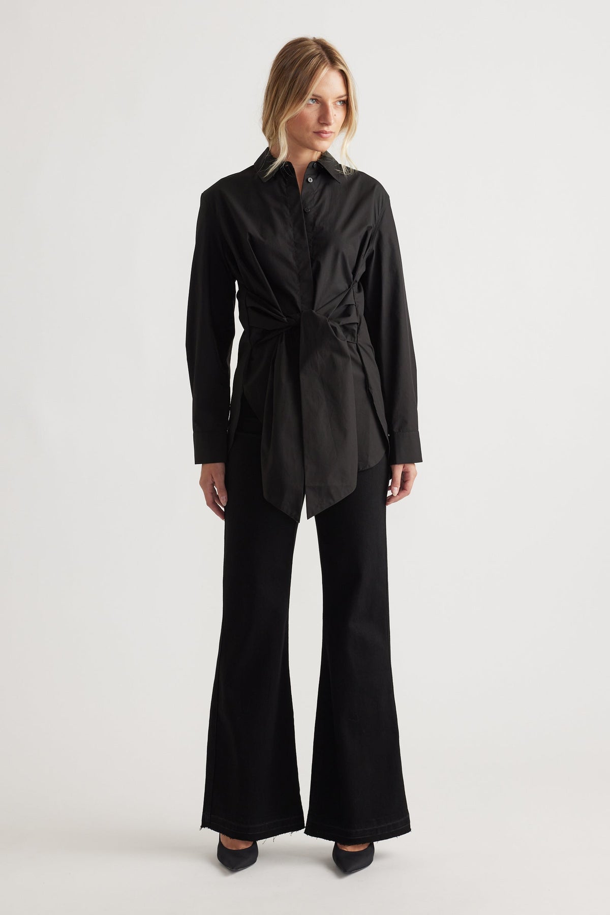 Woman wearing a sleek black tie-front shirt paired with high-waisted flared pants and pointed heels