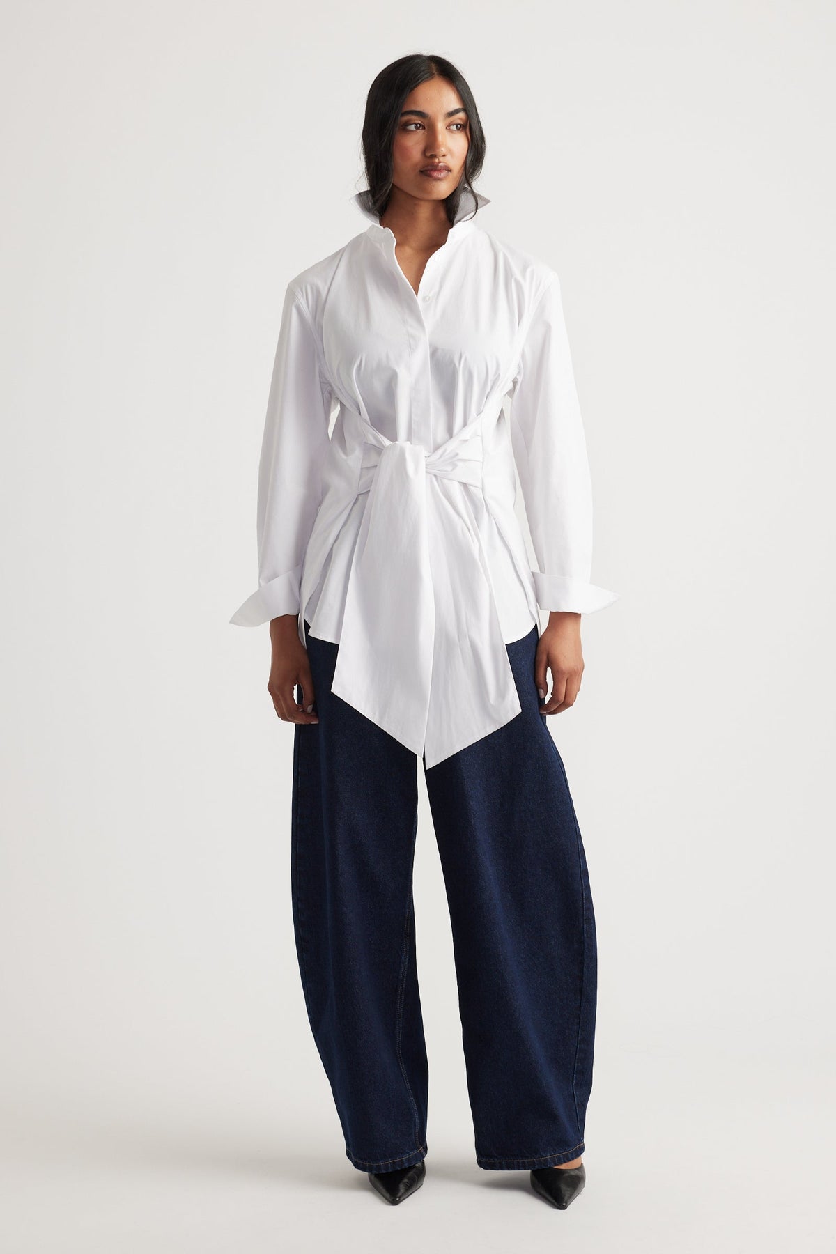 Woman wearing a white tie-front shirt paired with wide-leg dark denim jeans and black pointed shoes for a modern look