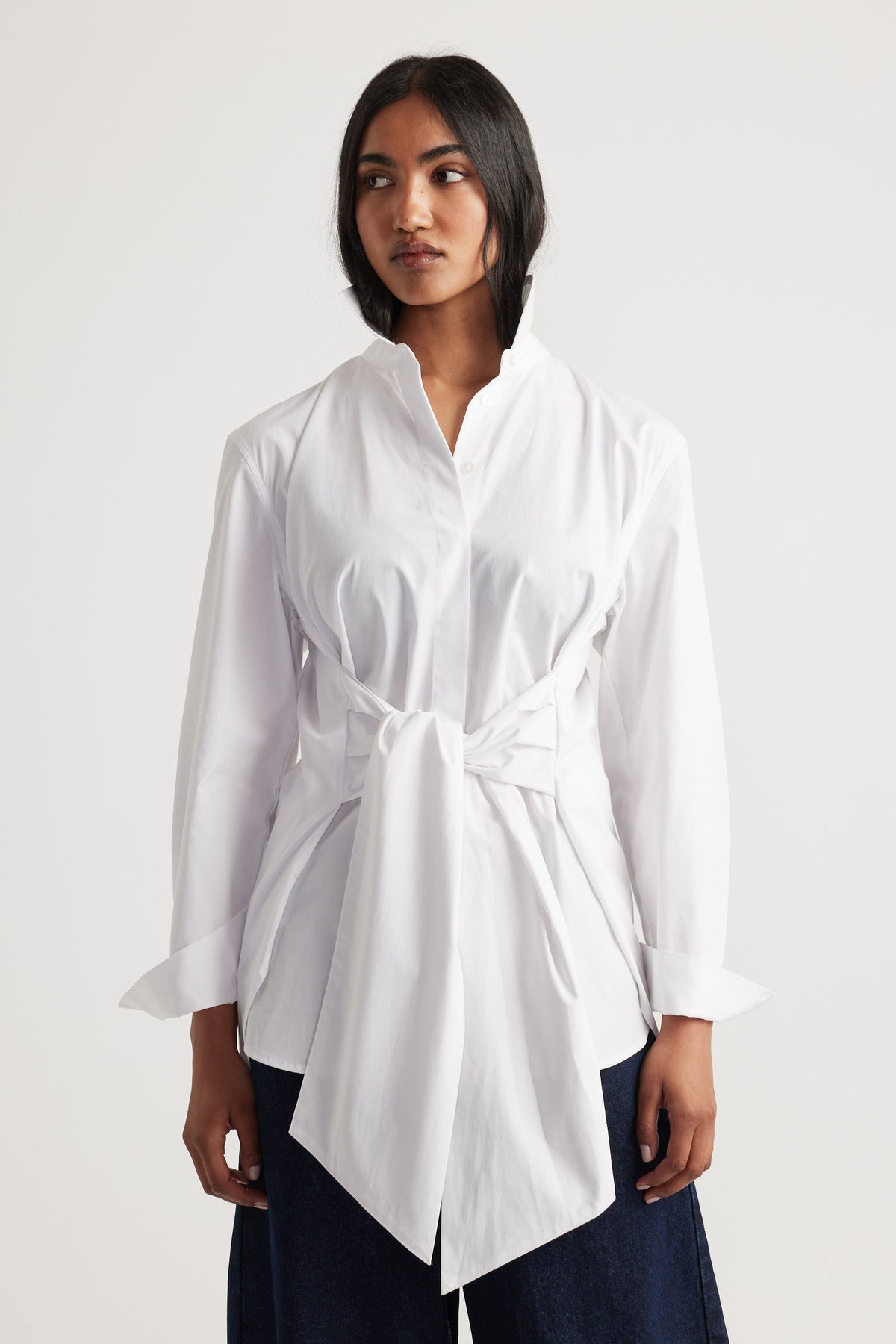 Woman wearing a white long-sleeve shirt with a tied waist detail paired with dark wide-leg pants.