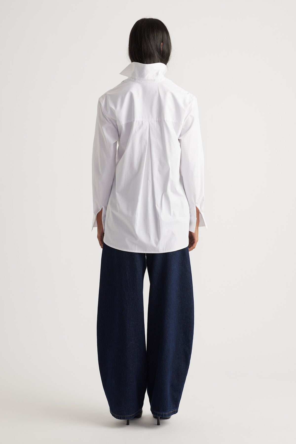 Back view of a woman wearing a crisp white tie-front shirt paired with wide-leg dark denim jeans and heels.