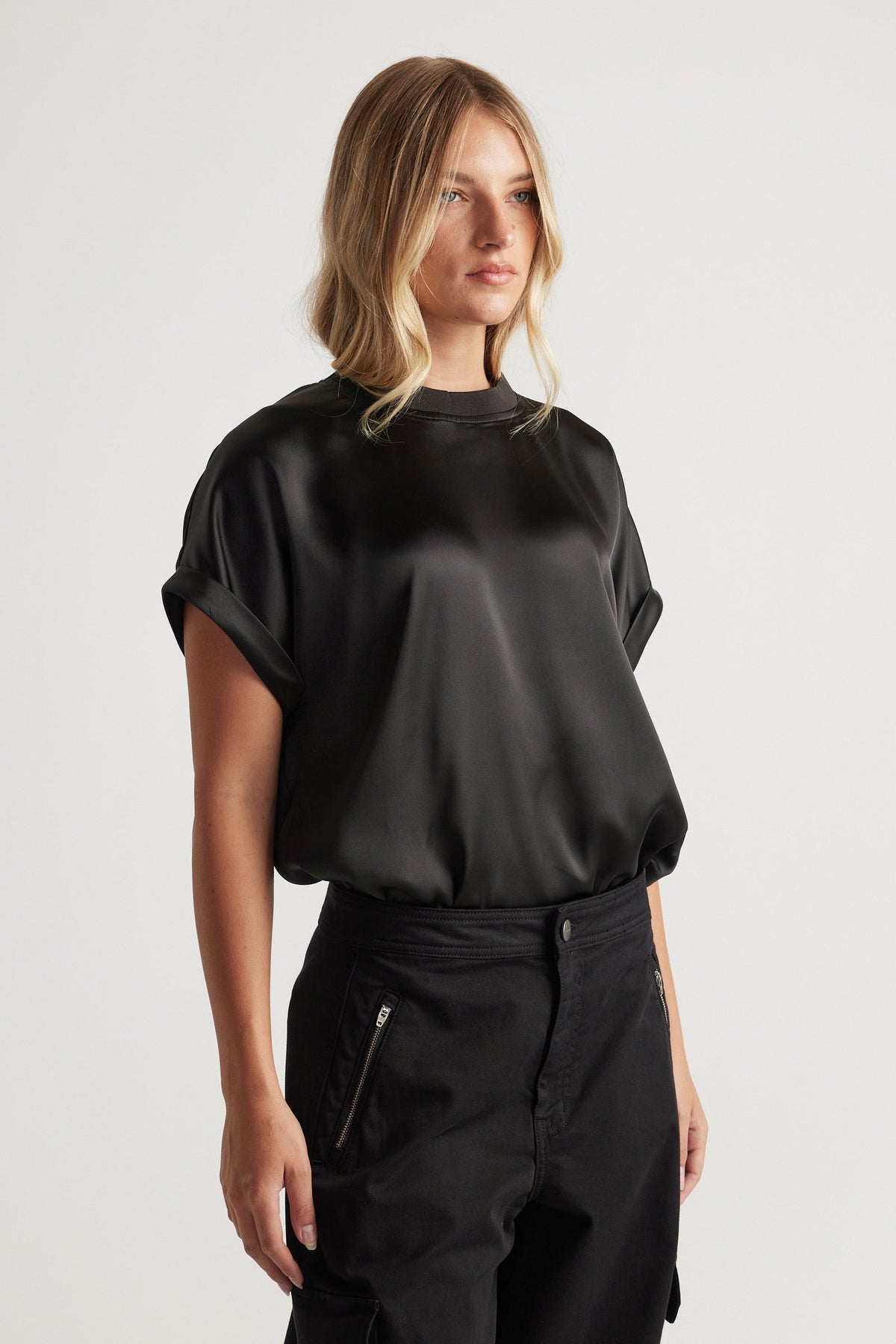 Woman wearing AnnMaree Satin Tee in black with rolled sleeves styled with relaxed black pants for a sleek look