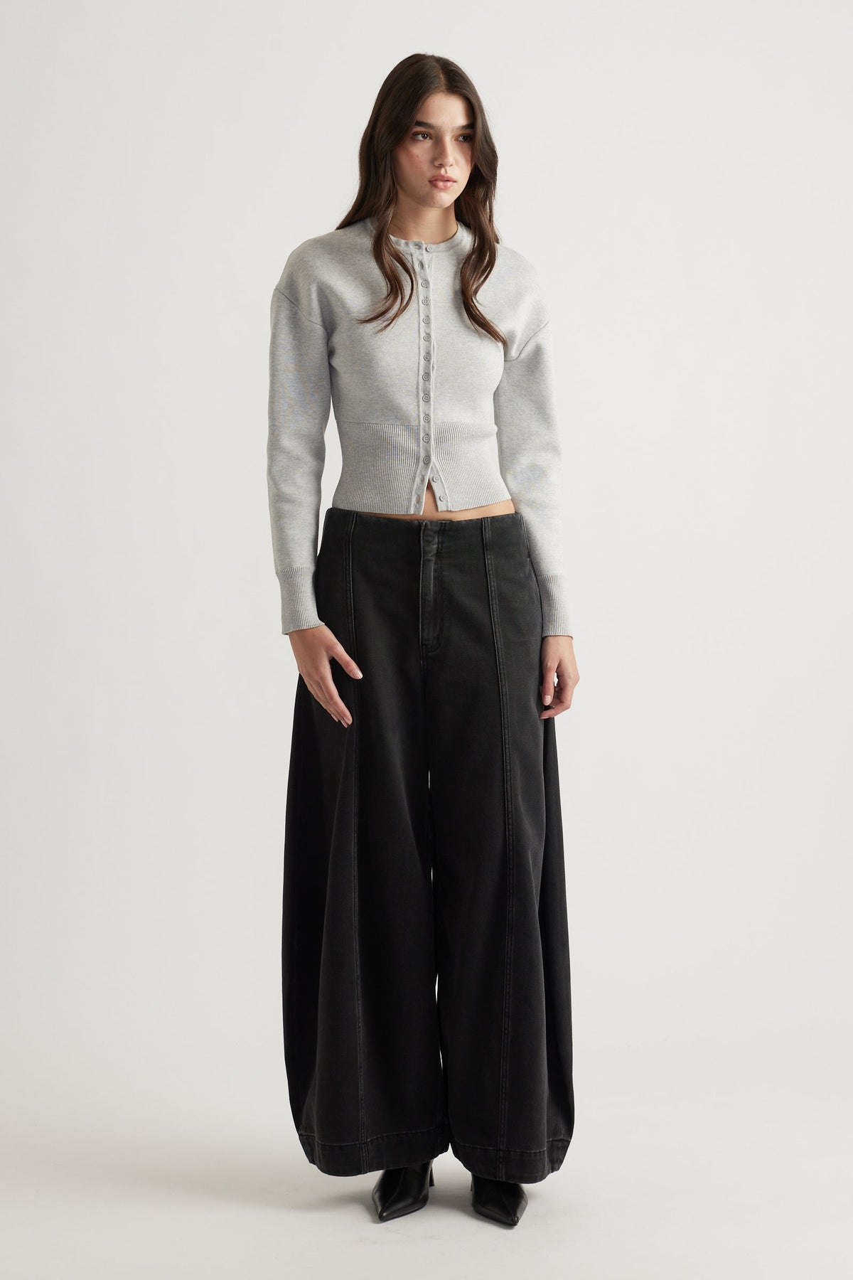 Woman wearing a light grey cinched knit cardigan paired with wide-leg black jeans and black pointed boots