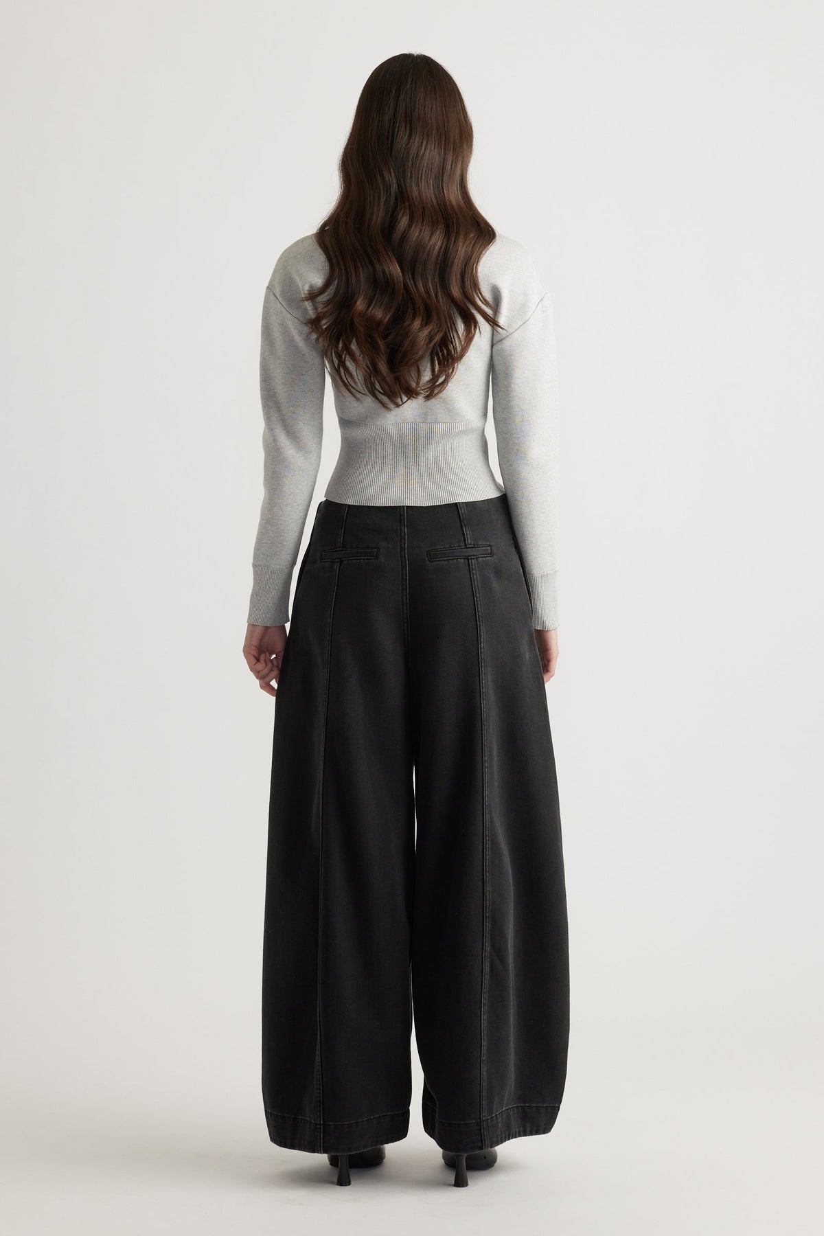 Back view of woman wearing a light grey fitted knit cardigan paired with wide-leg black pants and heels.