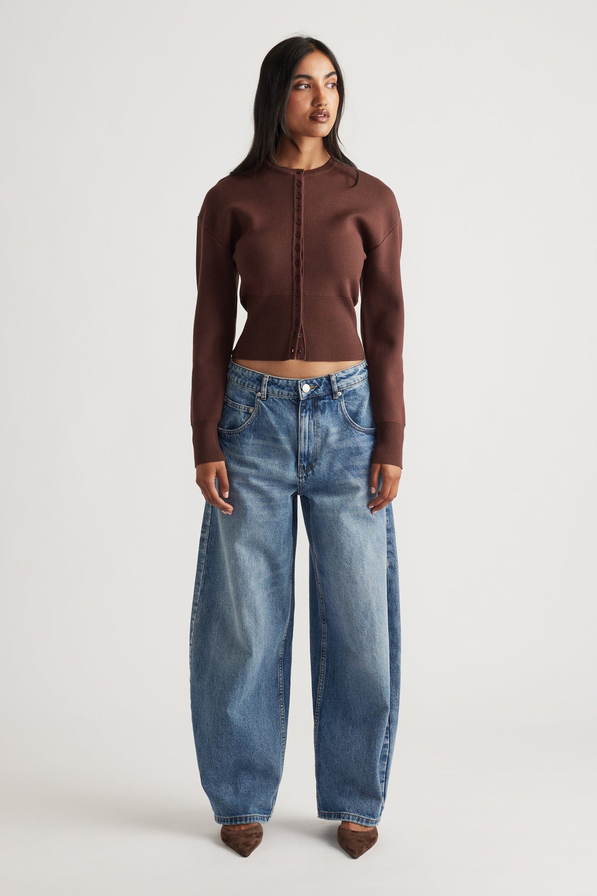 Woman wearing a fitted rich mocha cardigan with cinched waist paired with relaxed wide-leg blue denim jeans and pointed shoes