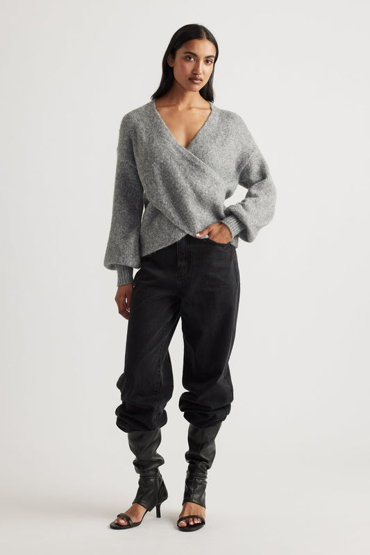 Woman wearing a soft grey crossover jumper styled with relaxed black jeans and black heeled boots for an easy chic look