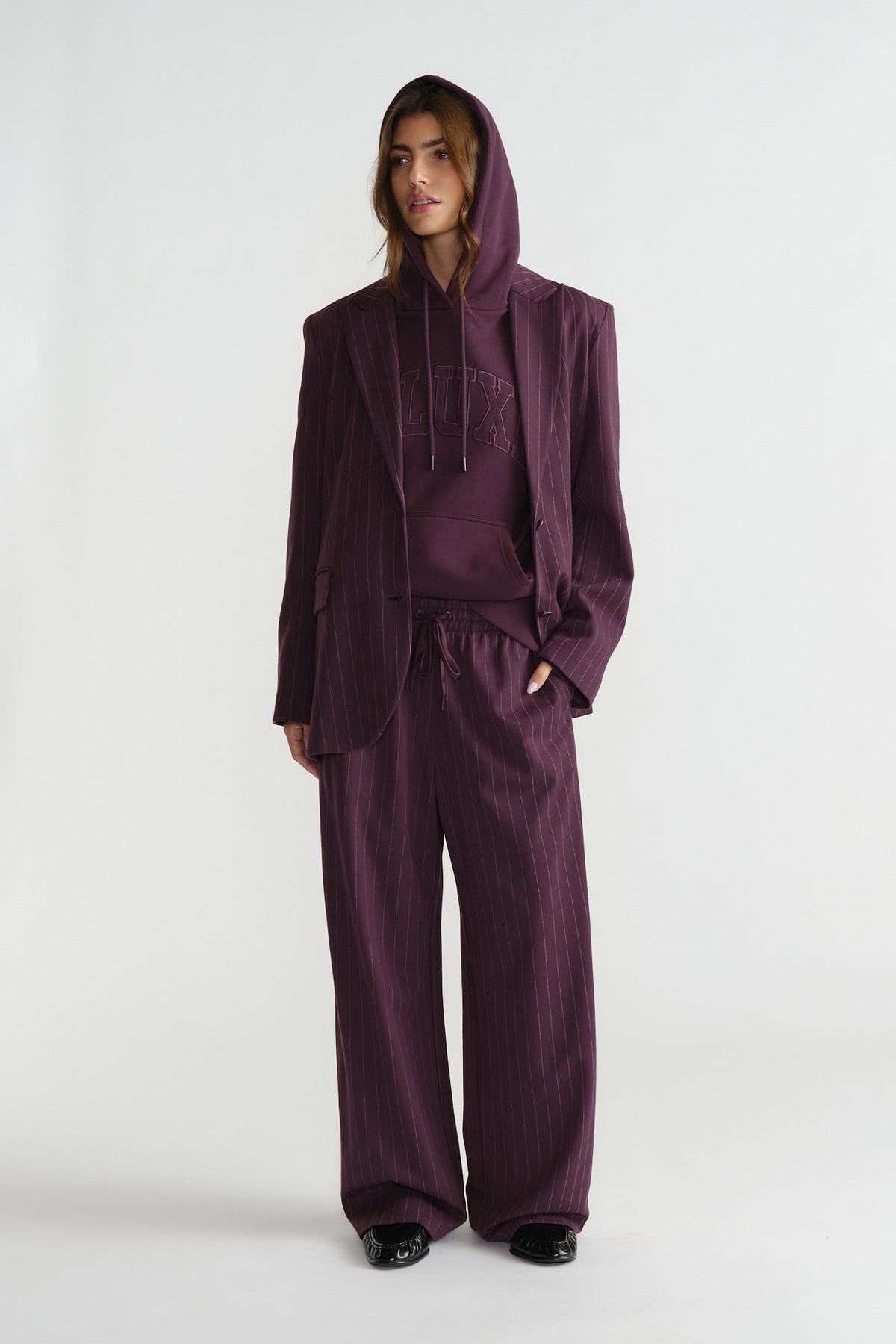 Woman wearing relaxed pinstripe pants and matching blazer layered over a hoodie in rich cherry tone