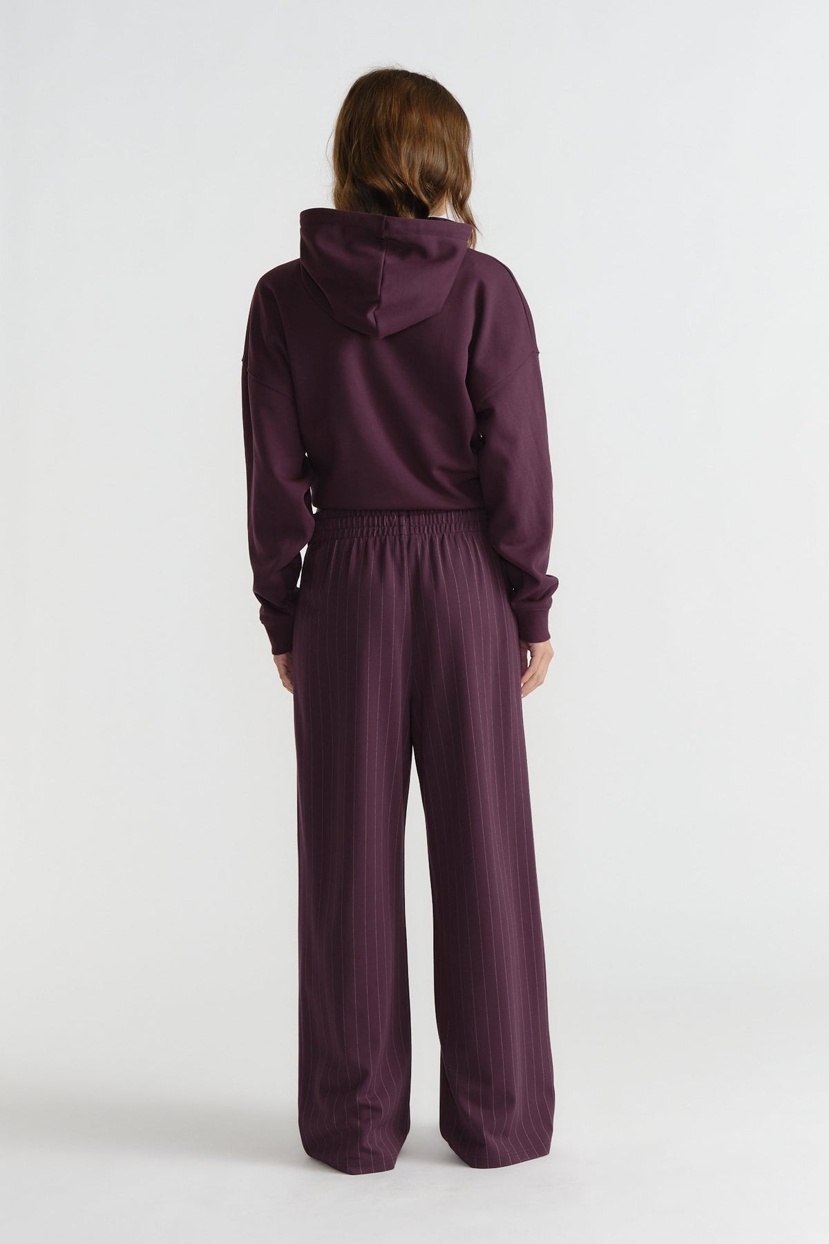 Back view of woman wearing relaxed-fit deep cherry pinstripe pants paired with a matching hooded top for a casual look