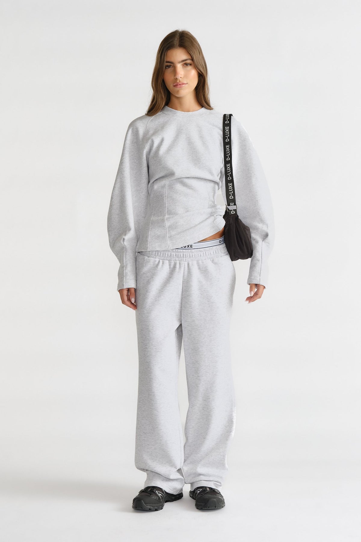 Woman wearing light grey cinched sweatshirt and matching relaxed sweatpants, styled with black shoes and a black shoulder bag