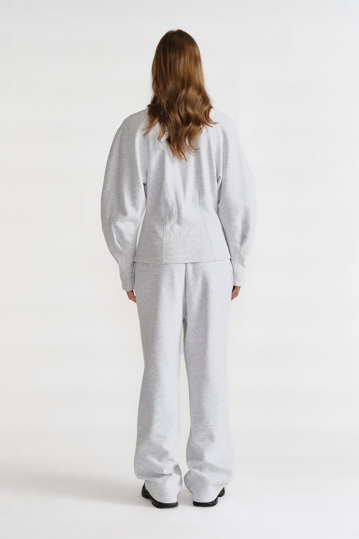 Rear view of a woman wearing light grey cinched sweatshirt and matching wide-leg sweatpants with black shoes